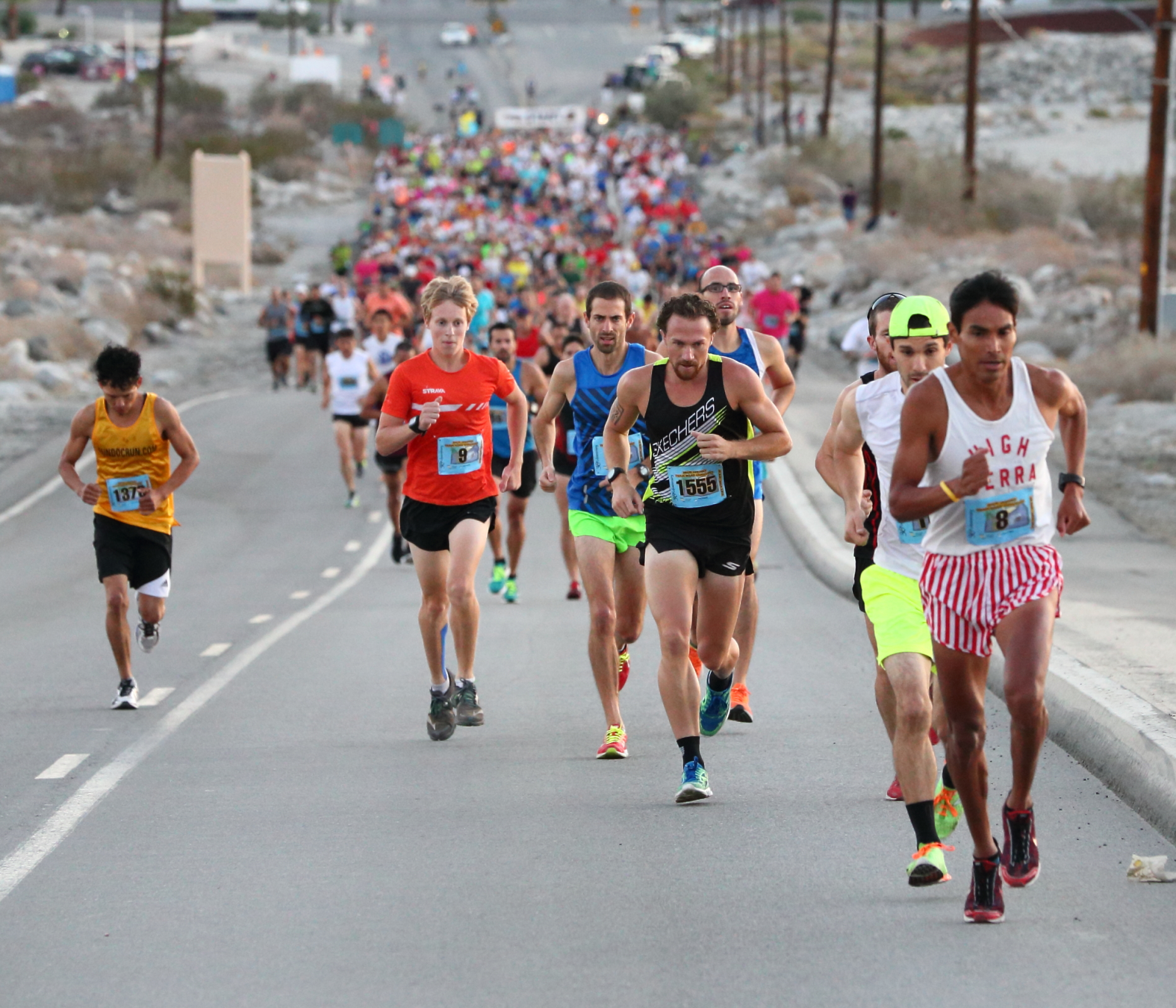Hundreds of runners in colorful clothing run up a steep pavement road.